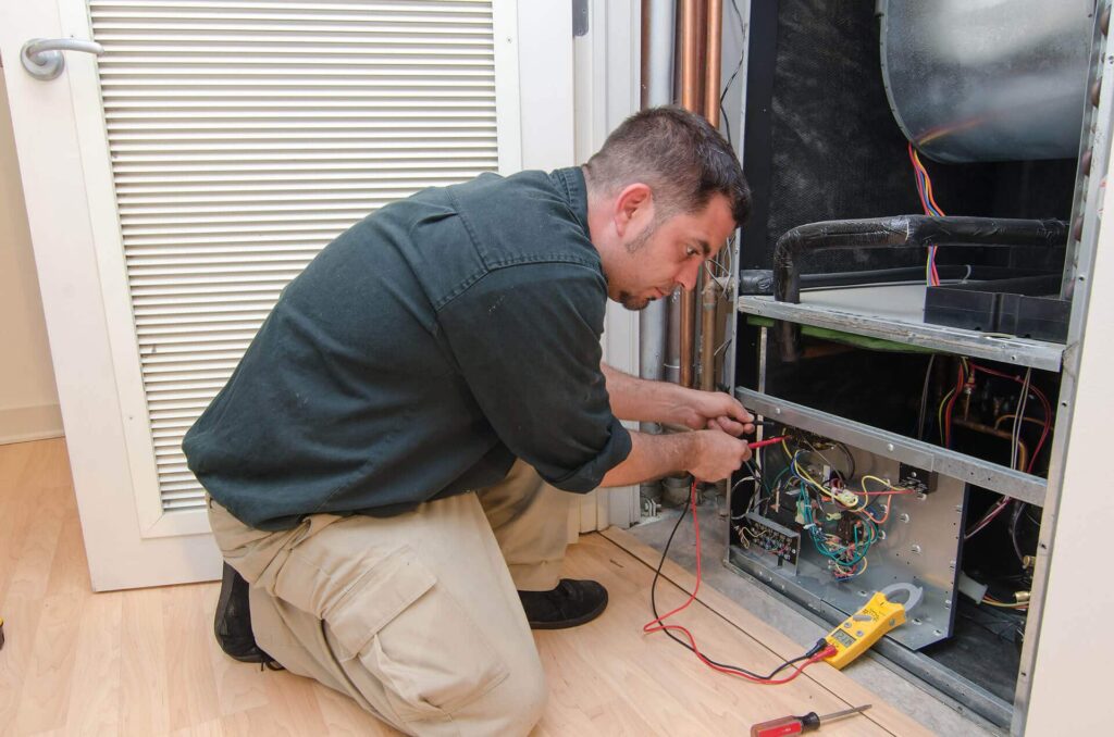 A picture of a Duggan's AC & Heating Technician repairing an indoor unit for the question "Is Ruud a Good Air Conditioner for All Seasons?"